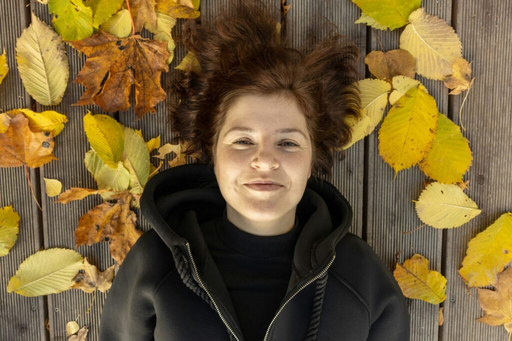 mujer sonriente recostada sobre hojas en otoño